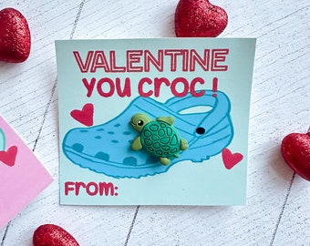 May include: Valentine's Day card with a blue and white cartoon croc shoe and a green turtle charm. The card says "Valentine you croc!" and "From:"