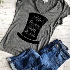 May include: A grey t-shirt with a black silhouette of a top hat and the text "A Million Dreams are Keeping Me Awake".