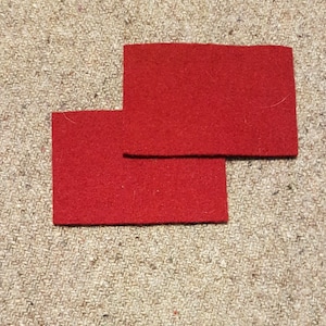 Peut inclure: Deux carrés de feutre rouge, l'un sur l'autre, sur une surface beige texturée.