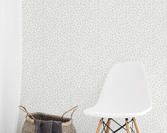 Puede incluir: Una silla blanca moderna con patas de madera se encuentra junto a una cesta tejida con una manta gris oscura. La pared está cubierta con un patrón de puntos gris claro y se ve una cortina blanca.