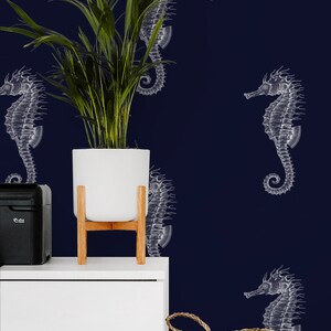 Peut inclure: Un mur bleu marine avec des illustrations d'hippocampes blancs. Un pot blanc sur un support en bois contient une plante verte. Une bo&icirc;te noire et un panier tress&eacute; sont sur une surface blanche.
