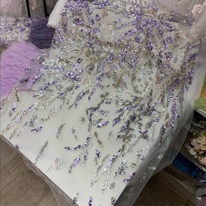 May include: A white sheer fabric with silver and purple sequins in a floral pattern.