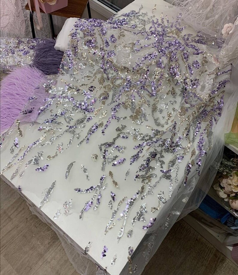 May include: A white sheer fabric with silver and purple sequins in a floral pattern.