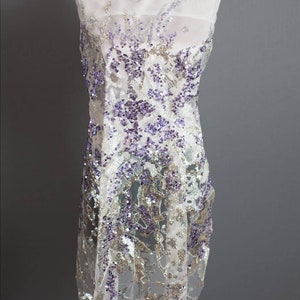 May include: White sheer fabric with purple and silver sequins in a floral pattern.