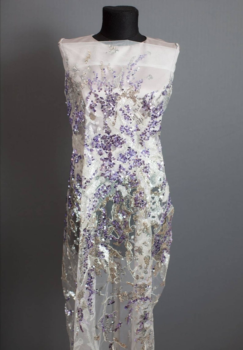 May include: White sheer fabric with purple and silver sequins in a floral pattern.