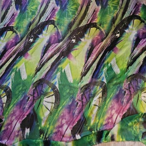 May include: Abstract printed fabric with a green, purple and black colour scheme. The fabric features a repeating pattern of stylised wheels.