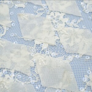 May include: Ivory lace fabric with a geometric pattern of overlapping squares. The fabric is embellished with small, iridescent sequins.