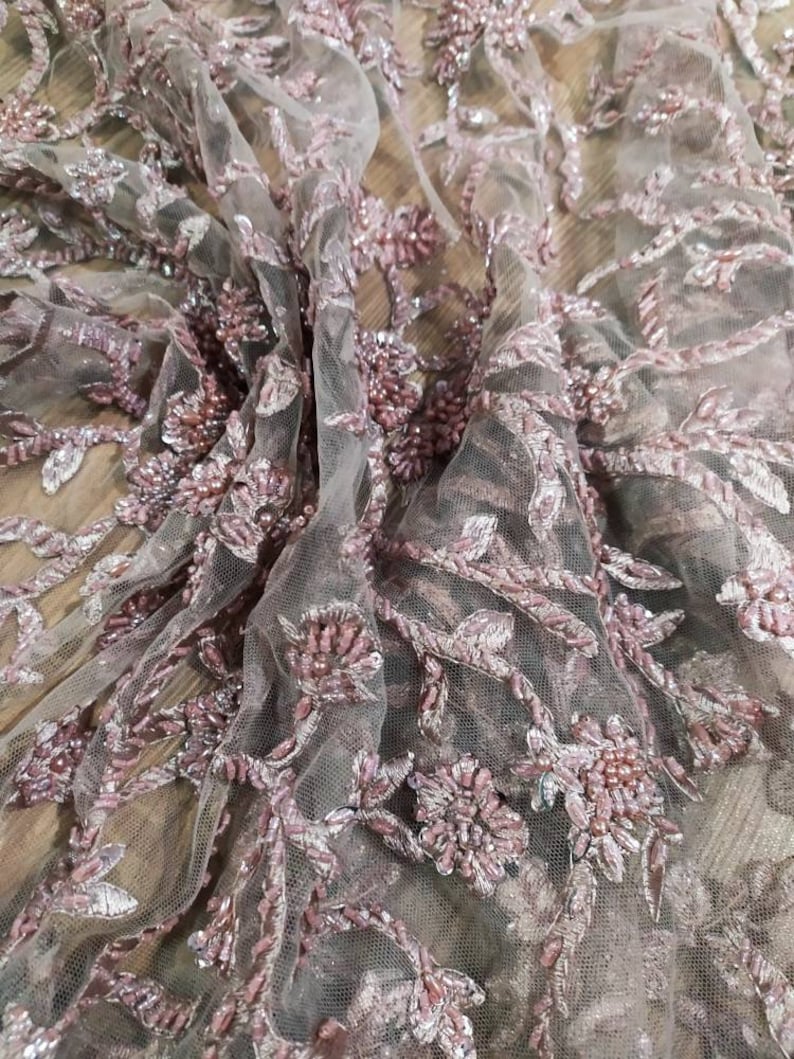 May include: Pink beaded lace fabric with a floral design. The fabric is sheer and delicate, with a soft, romantic feel.