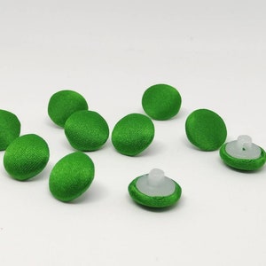 Op de afbeelding: Negen groene, met stof beklede knoppen met witte kunststof achterkanten. De knoppen zijn rond en hebben een glad oppervlak.