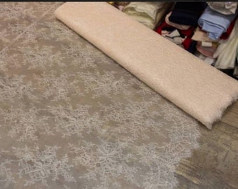 May include: A roll of delicate, white lace fabric with a floral pattern. The lace is on top of a roll of pale pink fabric.