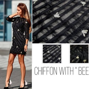 Puede incluir: Tela negra transparente con rayas horizontales y pequeñas abejas doradas. La tela está etiquetada "CHIFFON WITH "BEE"".
