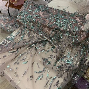 May include: A close-up of a sheer fabric with silver and teal sequins in a floral pattern.