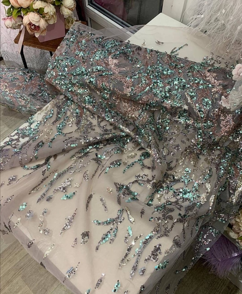 May include: A close-up of a sheer fabric with silver and teal sequins in a floral pattern.