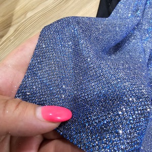 May include: Close-up of a blue fabric with silver glitter. The fabric has a textured, sparkly appearance.