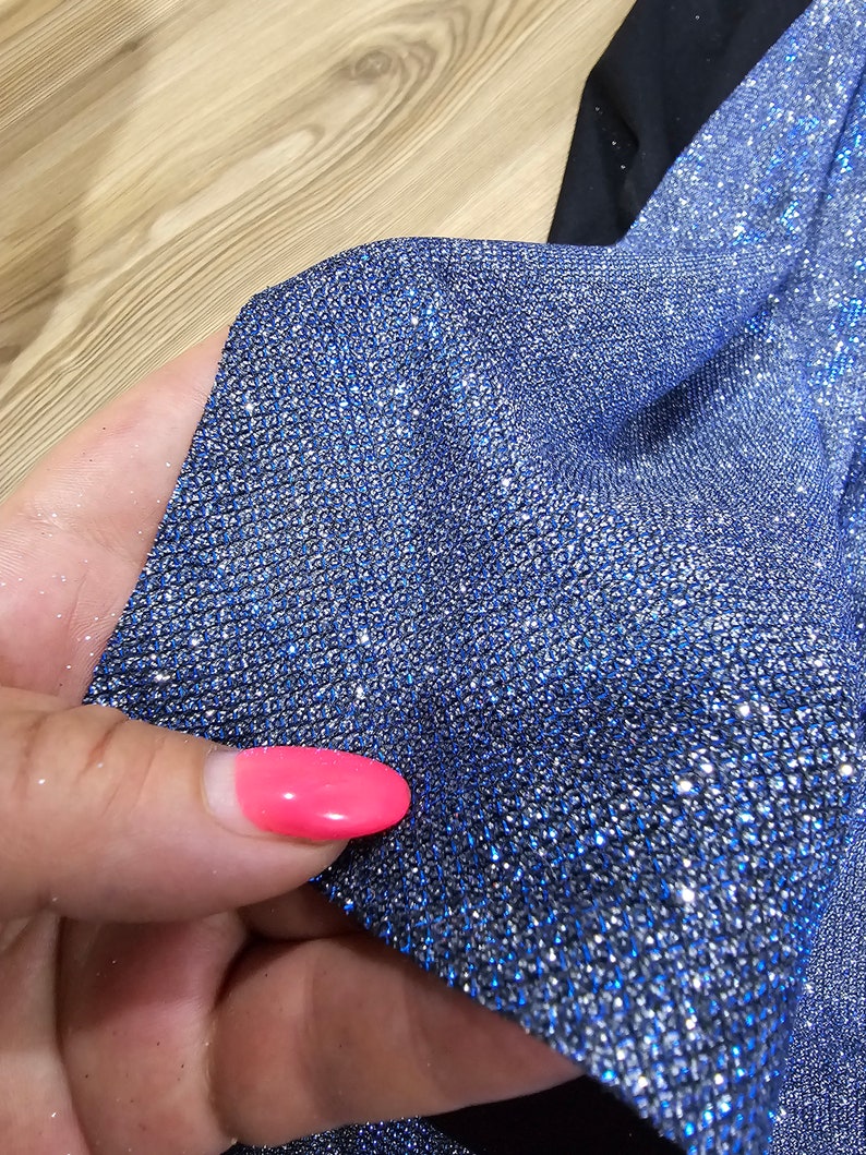 May include: Close-up of a blue fabric with silver glitter. The fabric has a textured, sparkly appearance.