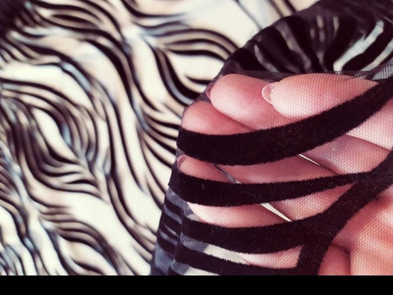 May include: Black velvet ribbon trim on sheer black fabric. The fabric is held in a hand.