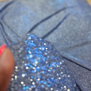 May include: Close-up of a blue fabric with a sparkly, glittery texture. The fabric is out of focus, creating a bokeh effect with small, round, blue and white lights.