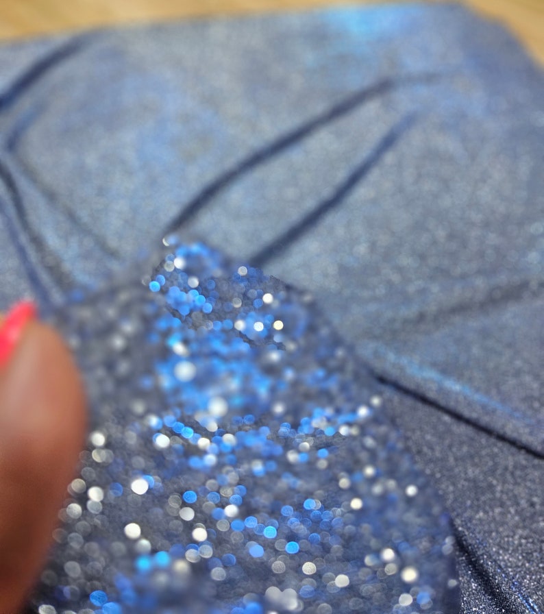 May include: Close-up of a blue fabric with a sparkly, glittery texture. The fabric is out of focus, creating a bokeh effect with small, round, blue and white lights.