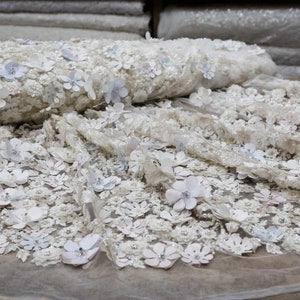 May include: White floral lace fabric with 3D flowers. The fabric is delicate and intricate, with a soft, romantic feel.