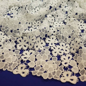 May include: White lace fabric with a delicate floral pattern. The lace is soft and flowing, with a subtle sheen.