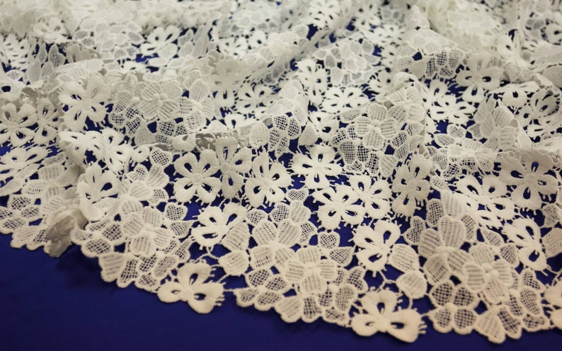 May include: White lace fabric with a delicate floral pattern. The lace is soft and flowing, with a subtle sheen.