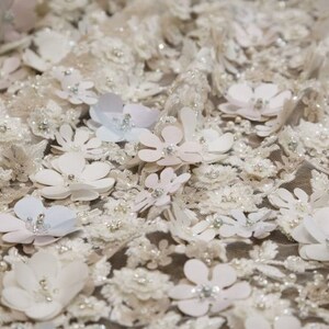 May include: White fabric with a delicate floral pattern. The fabric is covered in small, white flowers with a raised texture. The flowers are arranged in a random pattern and are interspersed with small, white beads.