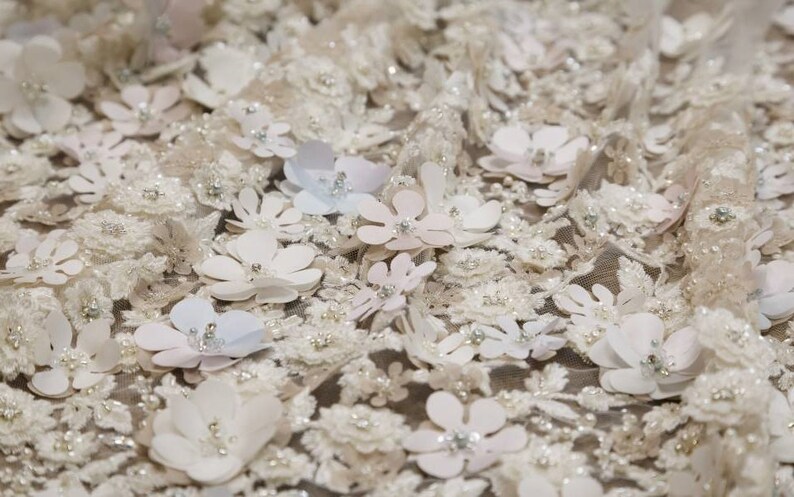 May include: White fabric with a delicate floral pattern. The fabric is covered in small, white flowers with a raised texture. The flowers are arranged in a random pattern and are interspersed with small, white beads.