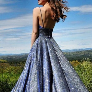 May include: A long, blue, sparkly, sleeveless dress with a V-neckline and a flowing skirt.