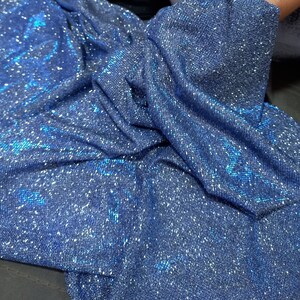 May include: A close-up of a blue fabric with a sparkly, iridescent finish. The fabric is wrinkled and has a textured surface.