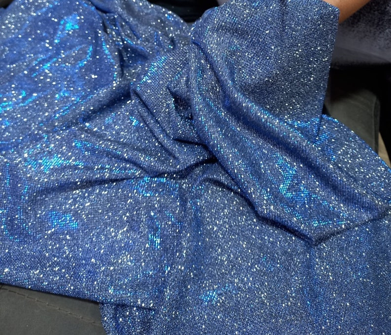 May include: A close-up of a blue fabric with a sparkly, iridescent finish. The fabric is wrinkled and has a textured surface.