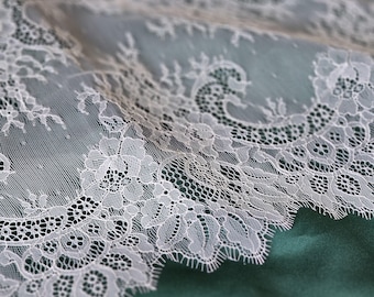 May include: White lace trim with a delicate floral pattern. The lace has a scalloped edge and is made of a fine, sheer fabric.