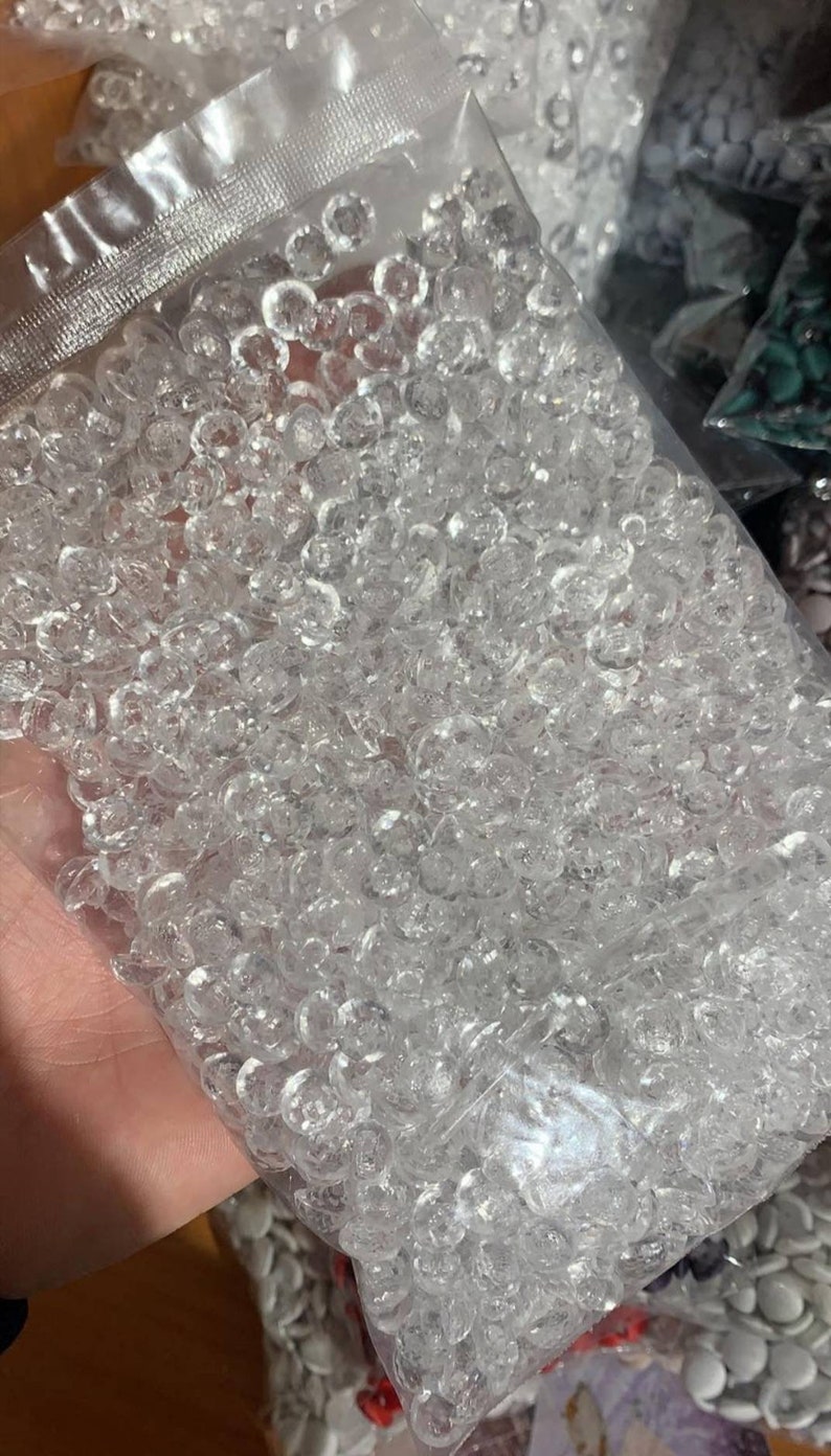 May include: A clear plastic resealable bag filled with a large quantity of small, round, transparent, faceted acrylic beads. Each bead features a multi-faceted surface that reflects light, creating a sparkling appearance throughout the collection.