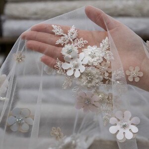 May include: White tulle fabric with delicate floral embroidery. The fabric features white and pink flowers with pearl accents.
