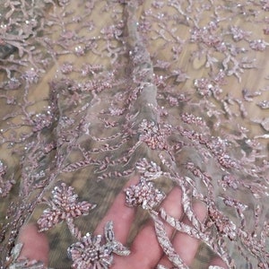 May include: Pink and silver beaded lace fabric with a floral pattern. The fabric is sheer and delicate, with a soft, shimmery finish.