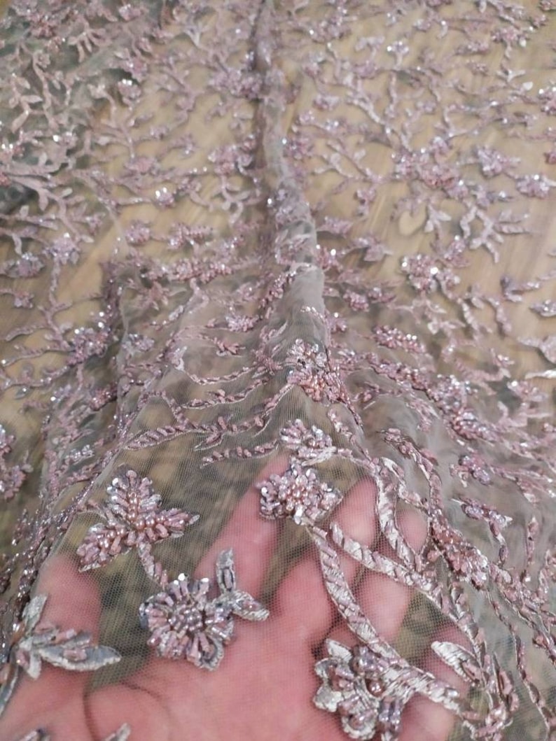 May include: Pink and silver beaded lace fabric with a floral pattern. The fabric is sheer and delicate, with a soft, shimmery finish.