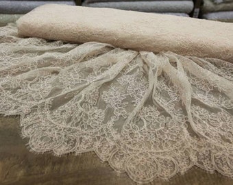 May include: A close-up of a delicate, off-white lace fabric with a floral pattern. The lace has a scalloped edge and is folded in half.