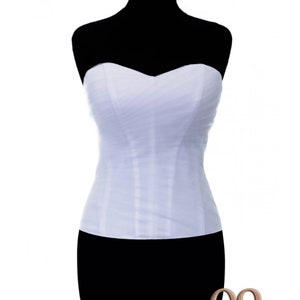 May include: White strapless corset with a sweetheart neckline. The corset is made of a soft, sheer fabric and has a fitted silhouette.
