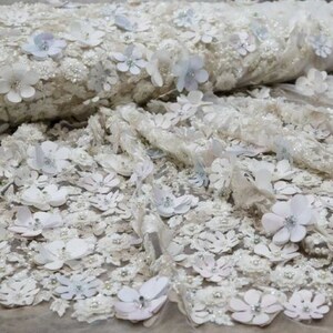 May include: White and light blue floral lace fabric with 3D flowers. The fabric has a delicate, sheer texture and is perfect for adding a touch of elegance to any project.