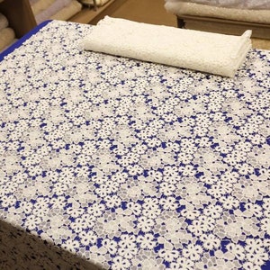 May include: White lace fabric with a floral pattern. The fabric is on a blue surface.