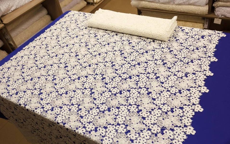 May include: White lace fabric with a floral pattern. The fabric is on a blue surface.