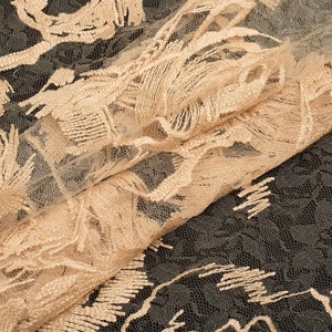 May include: Beige lace fabric with a delicate floral pattern. The lace has a textured, almost fringed, look.