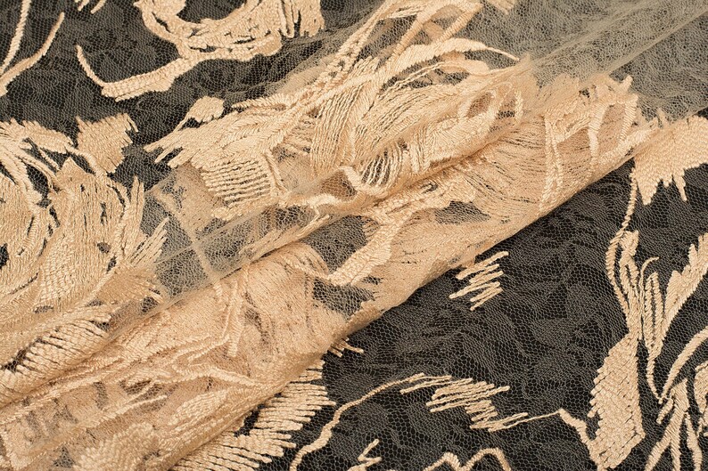 May include: Beige lace fabric with a delicate floral pattern. The lace has a textured, almost fringed, look.