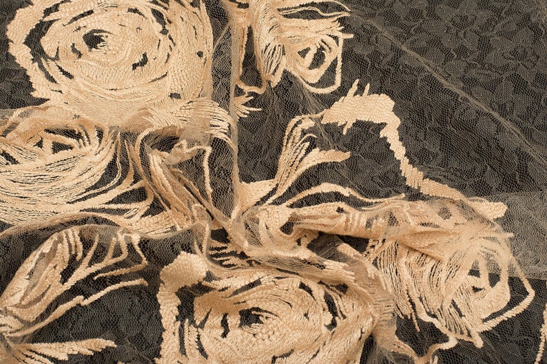 May include: Beige floral lace fabric with a delicate pattern of roses. The fabric is sheer and has a soft, flowing texture.