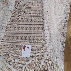 May include: White crochet fabric with a floral pattern. The fabric has a delicate, lacy texture and is perfect for crafting or sewing projects.