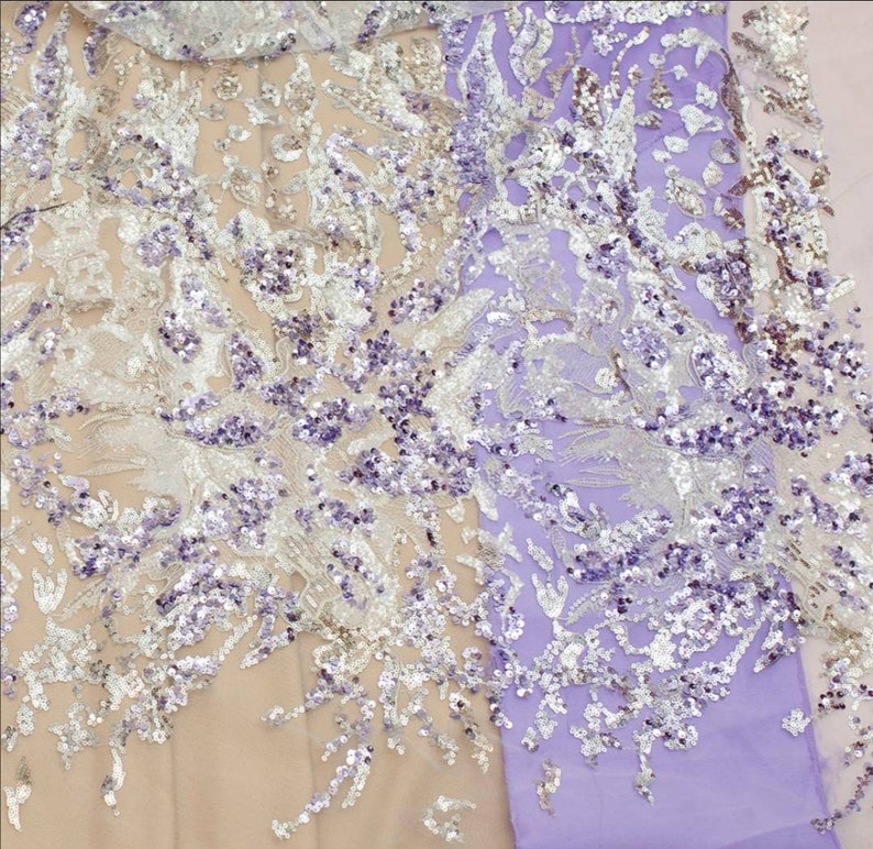 May include: A close-up of a sheer fabric with a floral pattern and silver and purple sequins. The fabric is a light purple color.