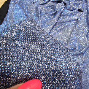 May include: Close-up of a blue sparkly fabric with a silver shimmer. The fabric is textured and has a subtle sheen.