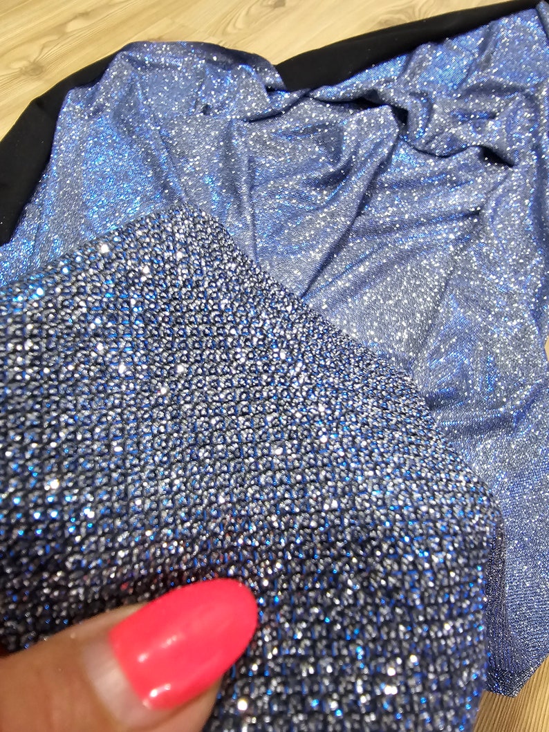 May include: Close-up of a blue sparkly fabric with a silver shimmer. The fabric is textured and has a subtle sheen.