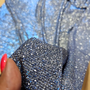 May include: Close-up of a blue fabric with silver glitter. The fabric is textured and has a shimmery finish.