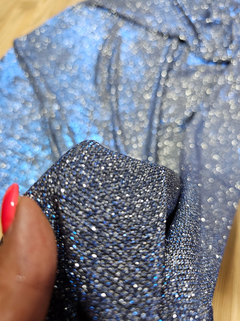 May include: Close-up of a blue fabric with silver glitter. The fabric is textured and has a shimmery finish.