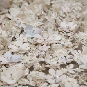 May include: White fabric with a delicate floral pattern. The fabric is covered in small, white flowers with a raised texture. The flowers are arranged in a random pattern and are interspersed with small, white beads.